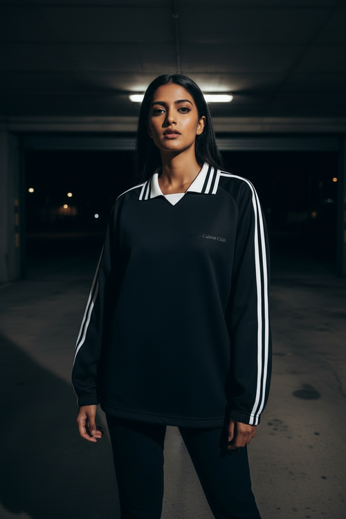 Divine Trio Hoodie model wearing a black sports style top with white stripes in an urban setting, showcasing sporty streetwear.